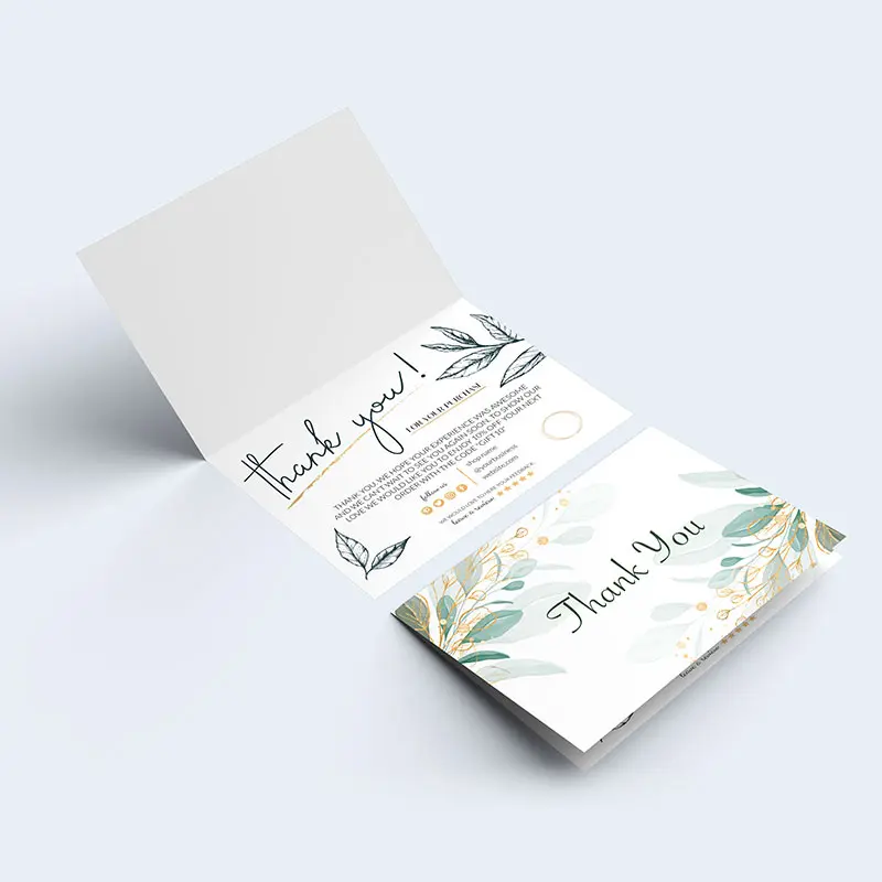 A thank you card is open on a light background, revealing two pages. The left page has a handwritten "thank you!" with decorative elements and text below. The right page, reminiscent of home, features florals in pastel colors and "Thank You" written in an elegant font.