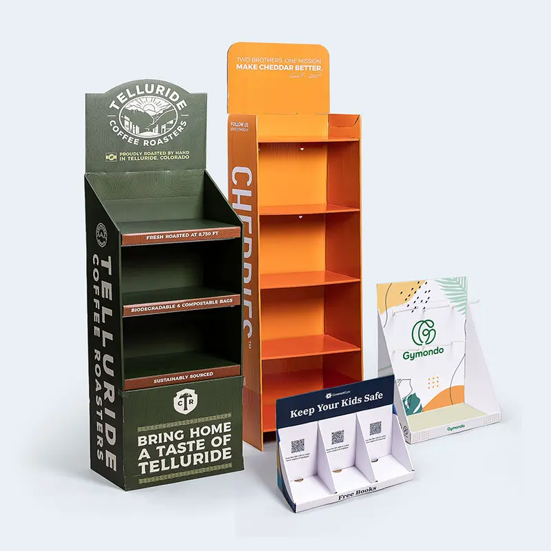 An assortment of cardboard retail displays includes a green Telluride Coffee Roasters stand, an orange Cherrio stand, a Gymondo display with a green logo, and a "Keep Your Kids Safe" stand featuring information slots with cards. Perfect for adding vibrant touches to your home or store.